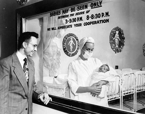 New father views child through nursery window in 1950.